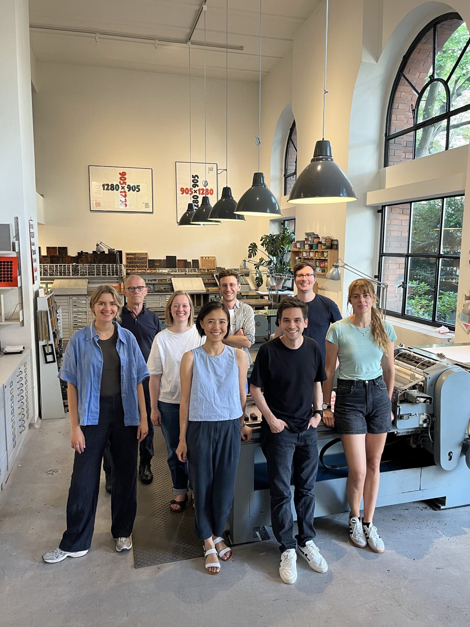 Group photo of the whole Village One team, Erik Spiekermann and Lilith standing around a letterpress printing machine, all smiling at the camera (except Erik, he looks uncharacteristically serious)