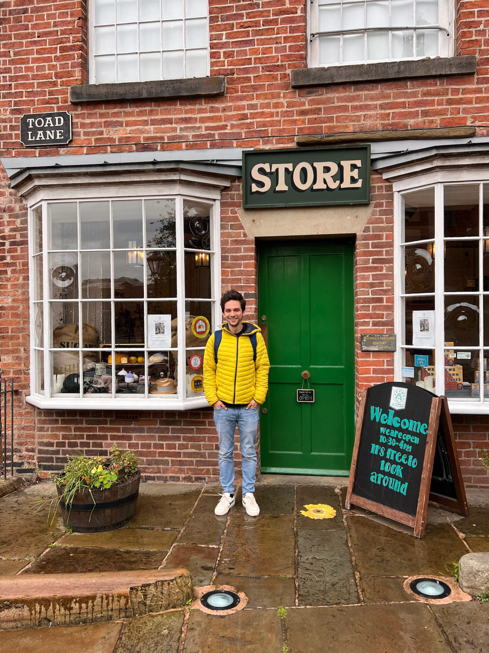 A dude in a colorful jacket standing in front of the Rochdale Pioneers store on a rainy day