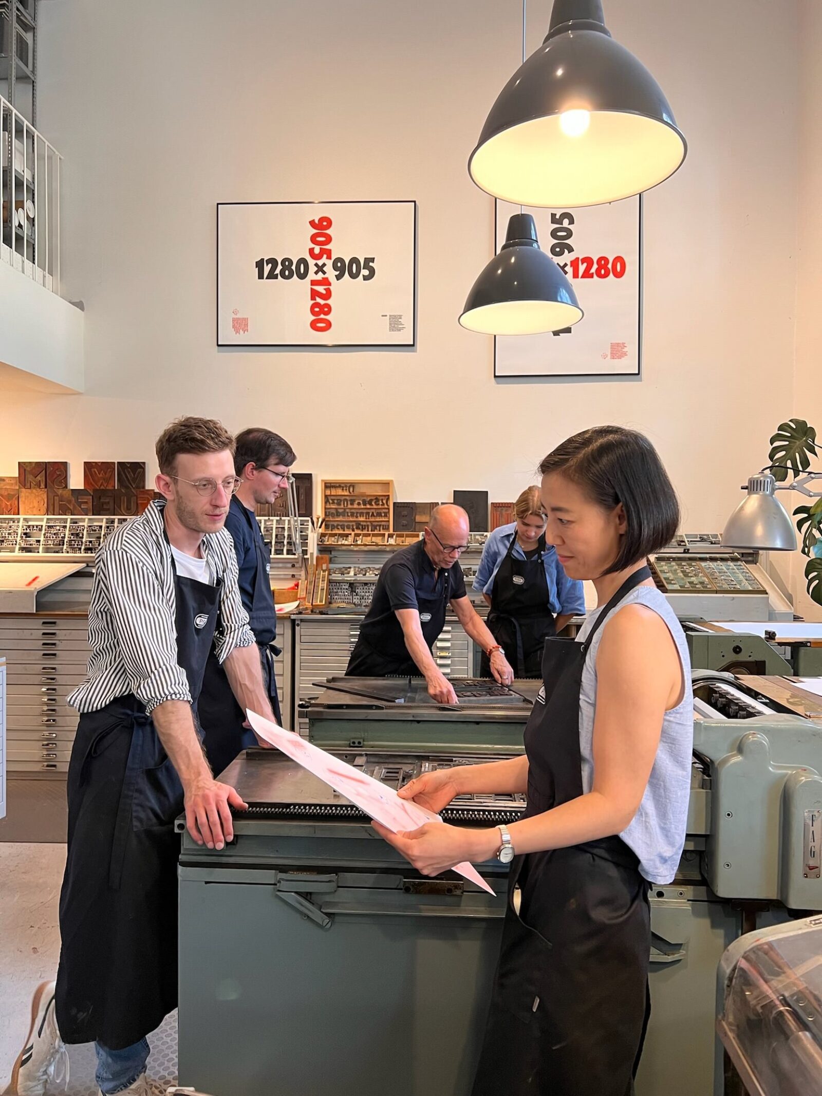 Photo of several people standing in a letterpress workshop, looking at posters