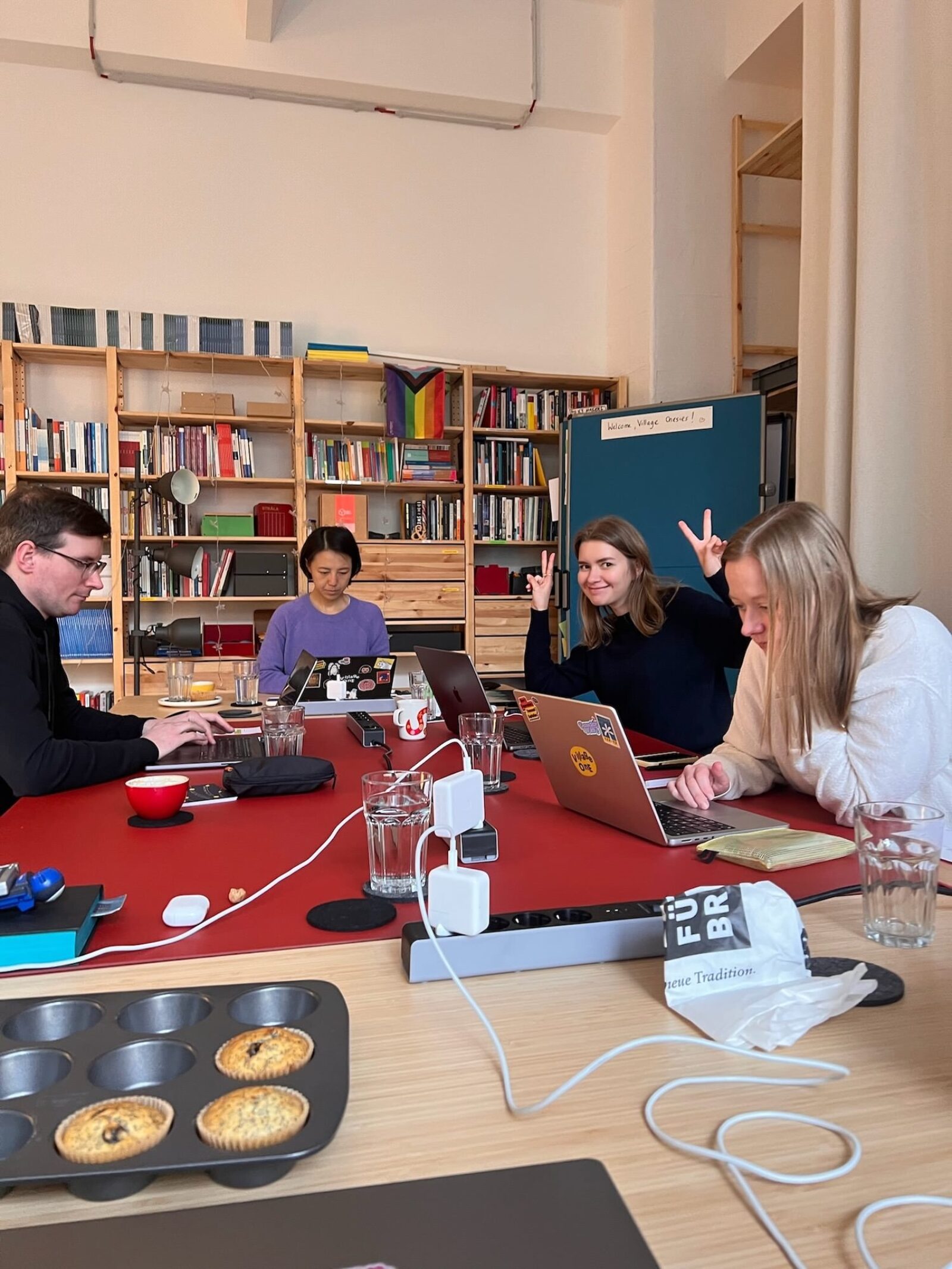 Four people from Village One sitting around a conference table, looking at laptops, one person showing the victory sign with their hands