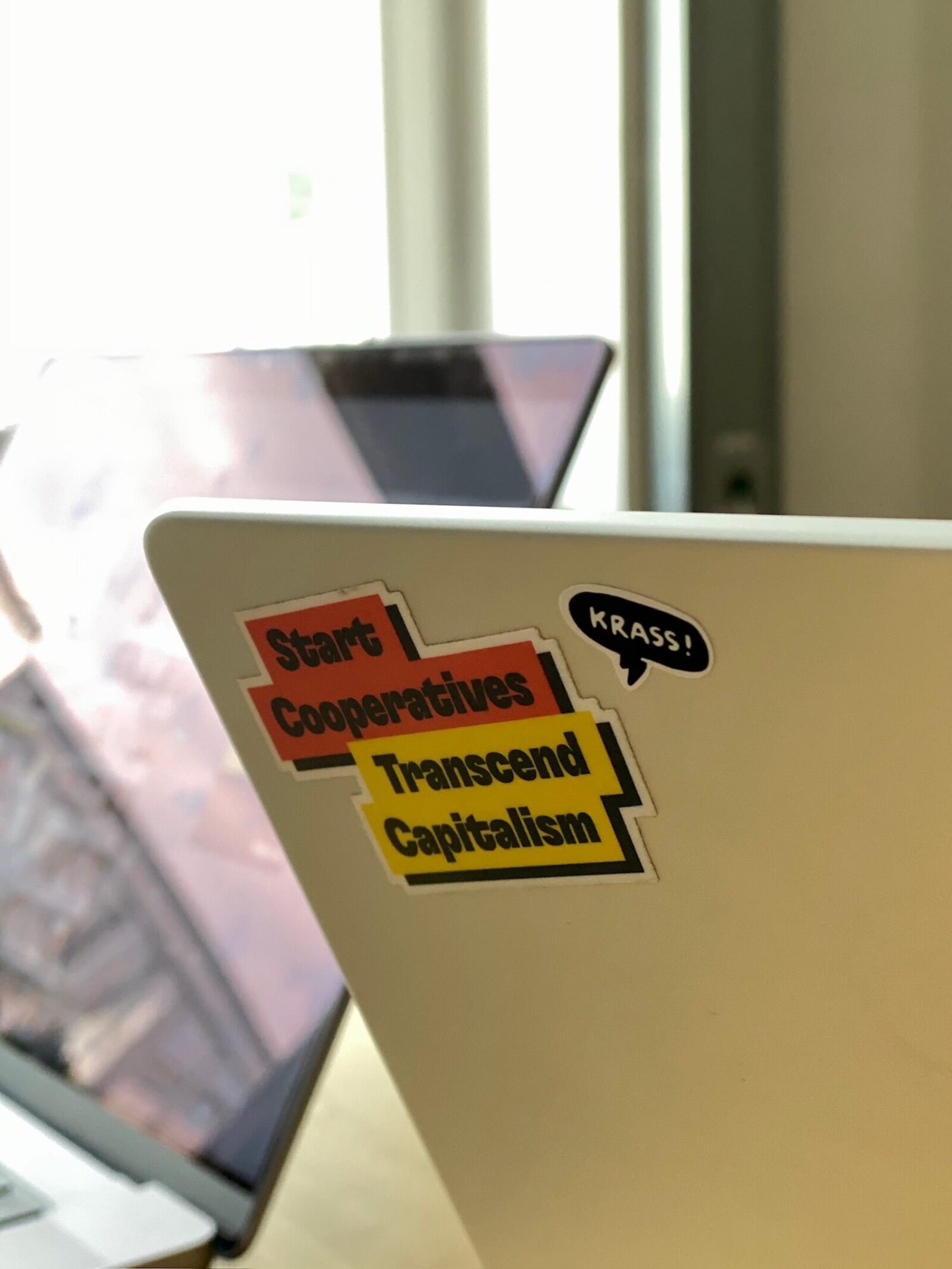 Photo of a laptop with stickers on it, stating “Start Cooperatives, Transcend Capitalism” and another one that says “Krass”