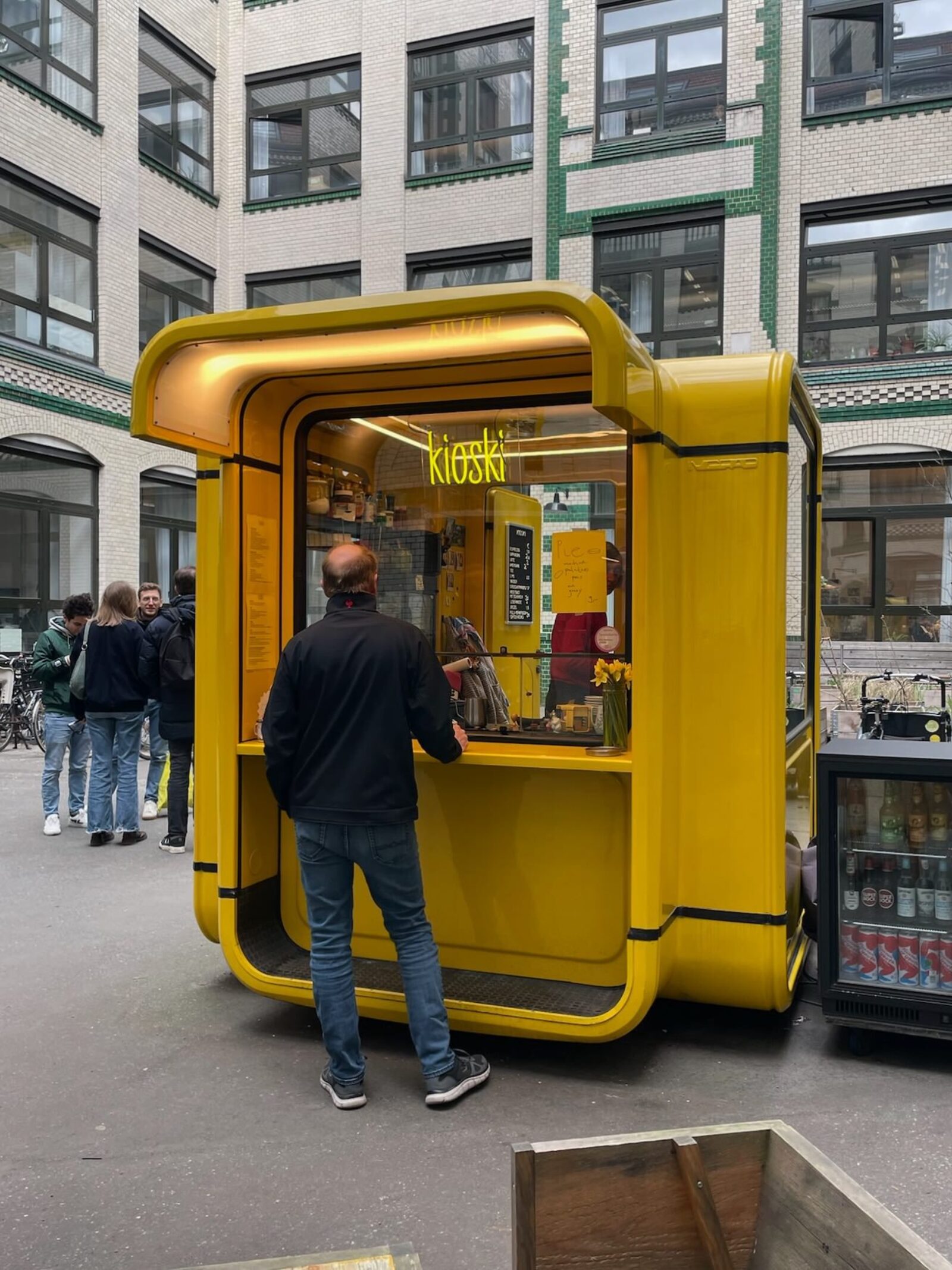 A small modular kiosk in a backyard in Berlin, with a person ordering some coffee