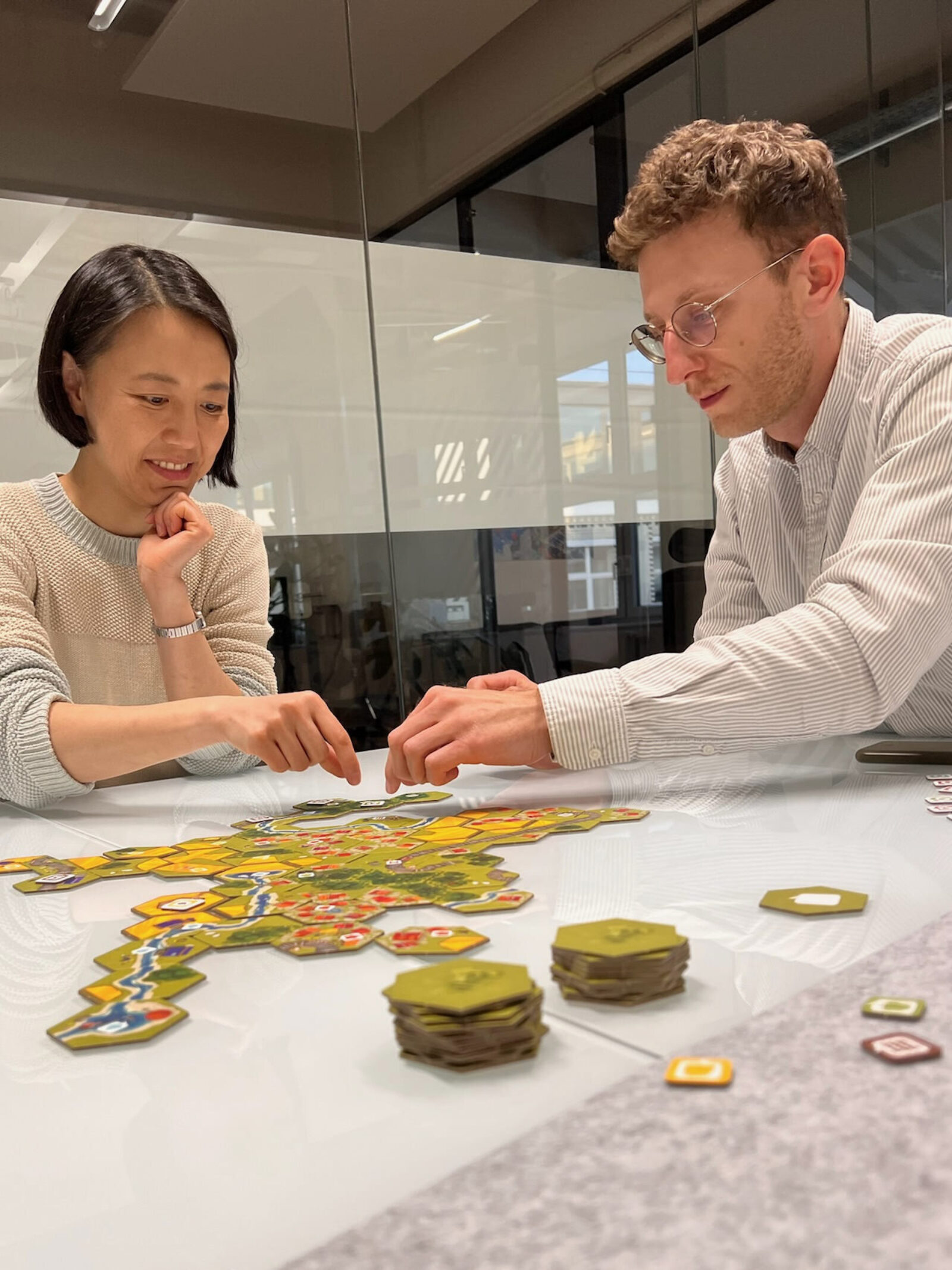 Two of us playing the board game “Dorfromantik” in a meeting room, staring at the game tiles with absolute focus