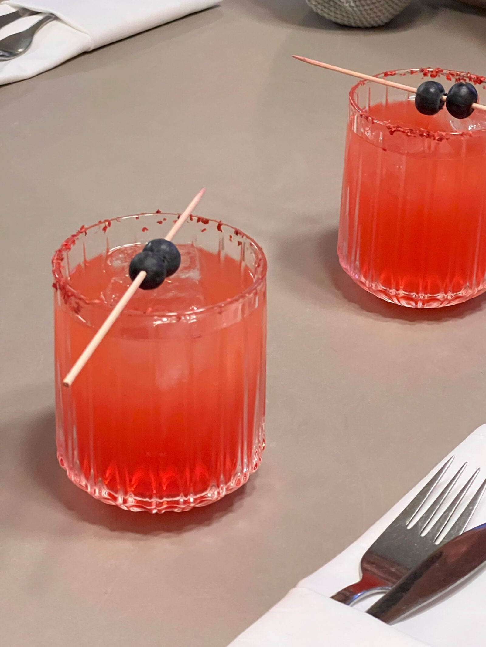 Photo of two colorful, fancy, alcohol-free drinks, on a table, with cutlery on the side