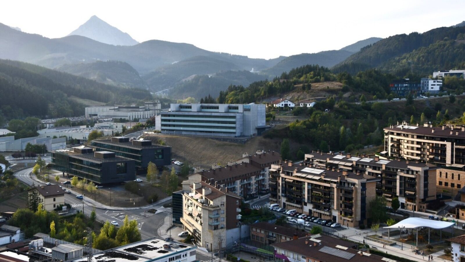 A photo of the mountainous landscape of Spain’s Basque region, with many modern buildings nestling into the hills, clear day, elevated camera position looking down at the city