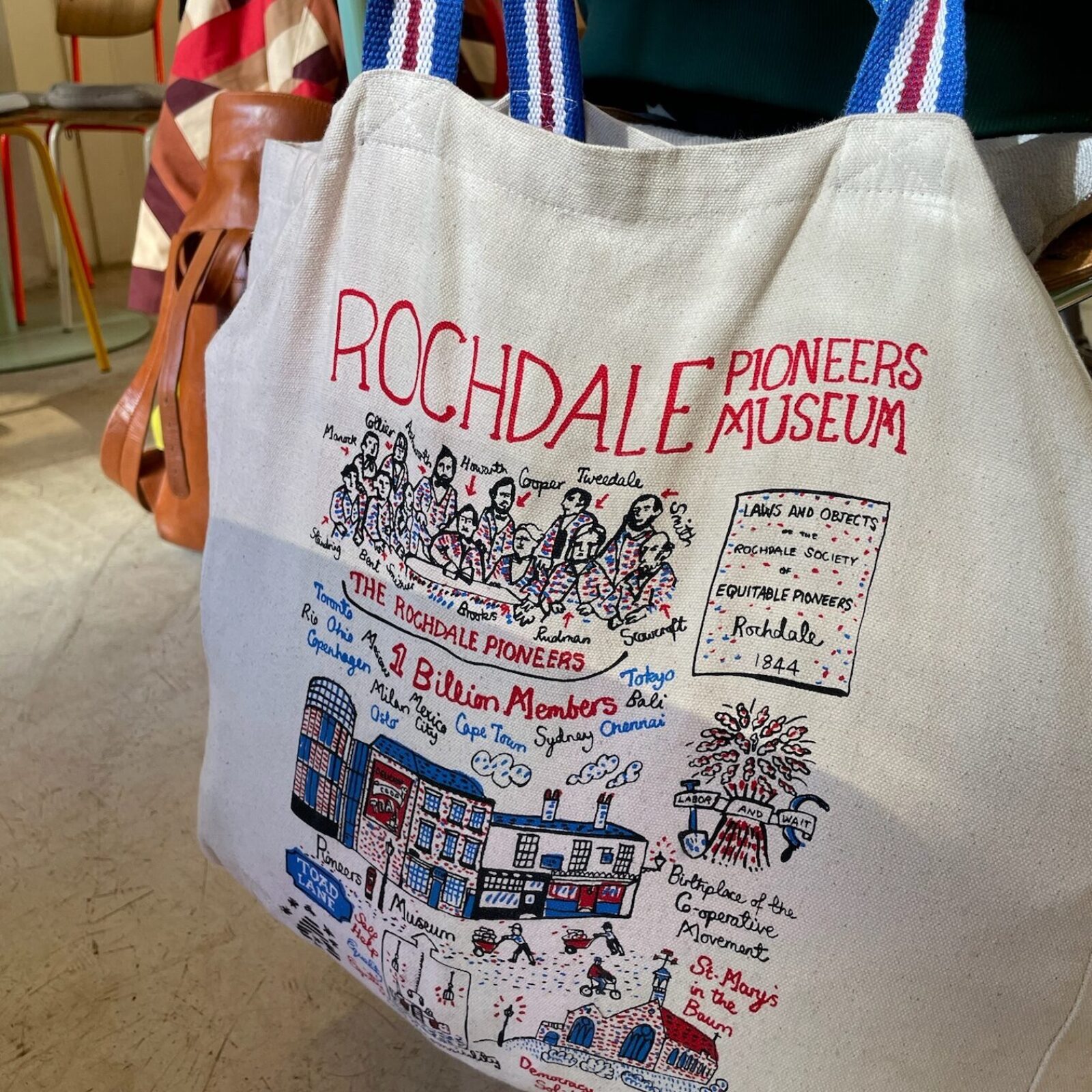 A photo of a tote bag with a colorful illustration about the “Rochdale Pioneers”, bought from the eponymous museum