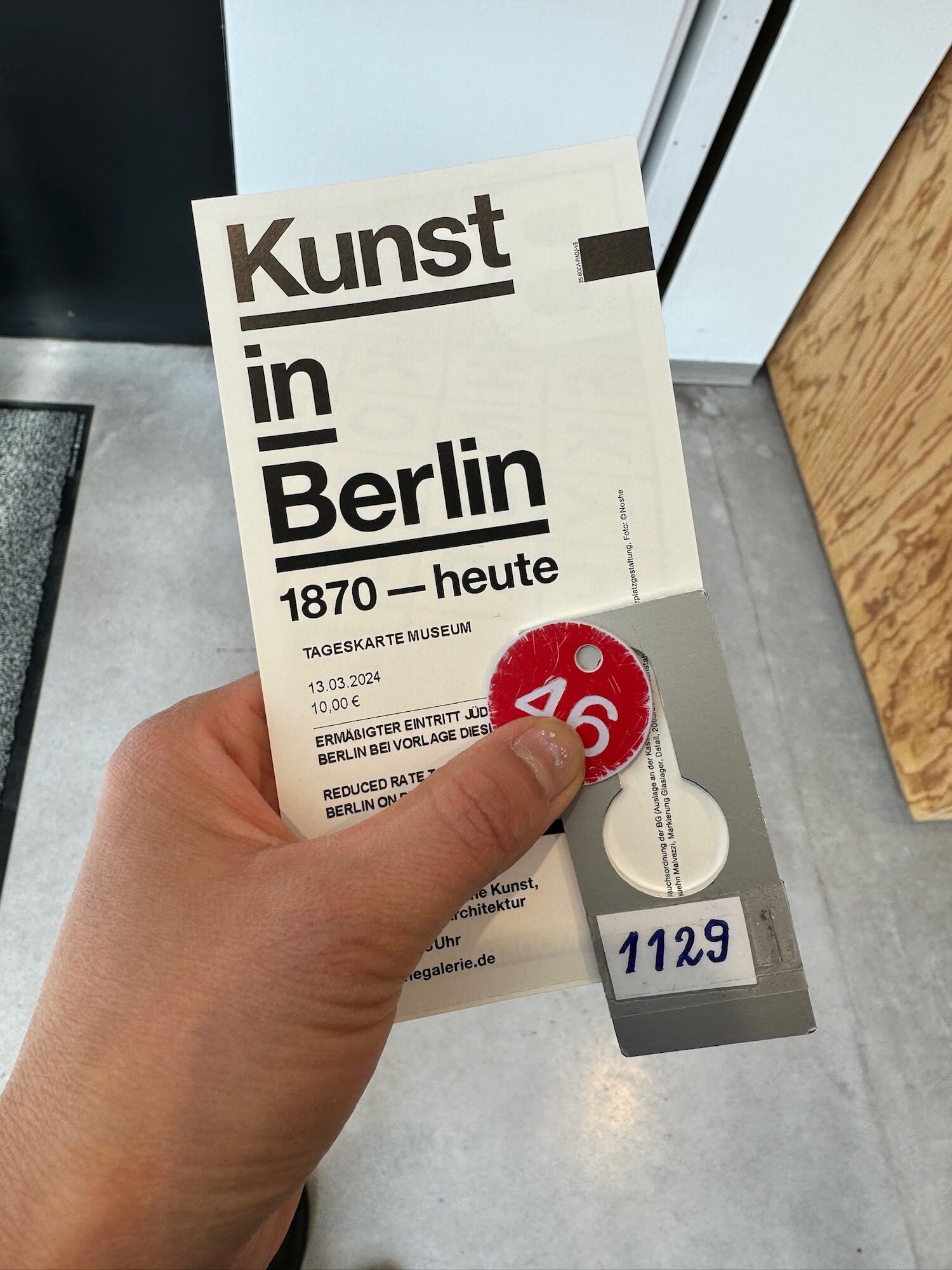 A hand holding a ticket to Berlinische Galerie and locker their room tags. The ticket says “Kunst in Berlin, 1870-heute”